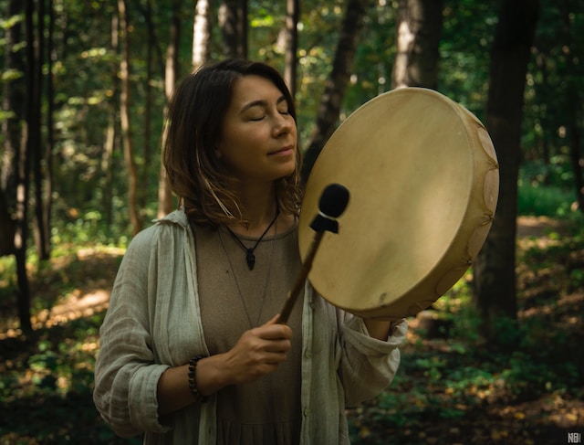 A woman playing a tambourine in the forest